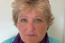 A woman with short blonde hair wearing a turquoise top with a purple scarf.